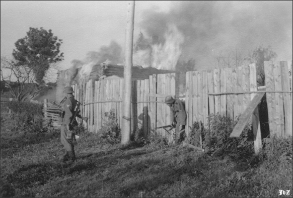 A light MG-34 team advances through a whole in a fence following the seizure of Krassny in the Soviet Union, August 1941.  The soldier (schütze 2) passing through the fence carries a box of ammunition and his rifle, while his partner (schütze 1) stands with the MG-34 slung over his shoulder.  The gunner also carries a box of ammunition in his left hand and a spare barrel in its carrying case slung over his shoulder.