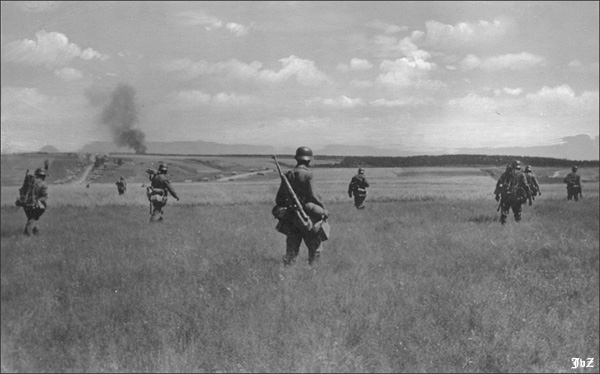 Heavy machine gun teams advance through a field in the Soviet Union.  Two of the soldiers appear to be carrying the MG-Lafette 34 tripod on their backs, others are carrying boxes of ammunition and the MG-34 itself.