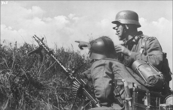A light machine gun team prepares to position themselves for action on the Eastern Front.  The gunner crouches below the crest of the rise holding the MG-34, while the section leader and another soldier look over the top and appear to check the position’s field of fire.  The gunner has added a few scattered leaves to the webbing on his helmet in an attempt to add some camouflage.