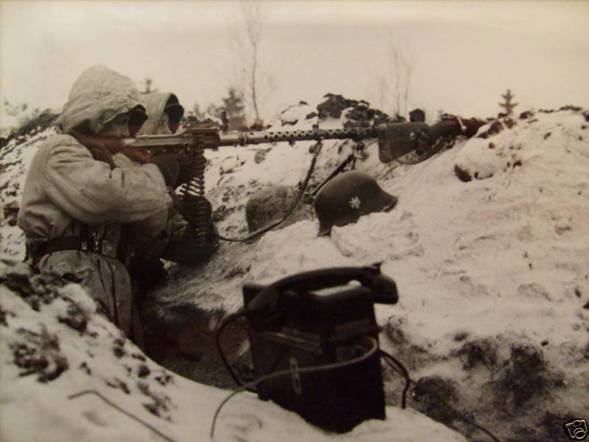Crew of a machine gun MG 34 in their role as light weapon, somewhere in the eastern front. It can be seen as the gunner Nº 2 presented the ammo band and to their right a rifle mauser K98k placed in the main firing direction. In the bottom of the photograph a field telephone that links the position with the Platoon HQ.
